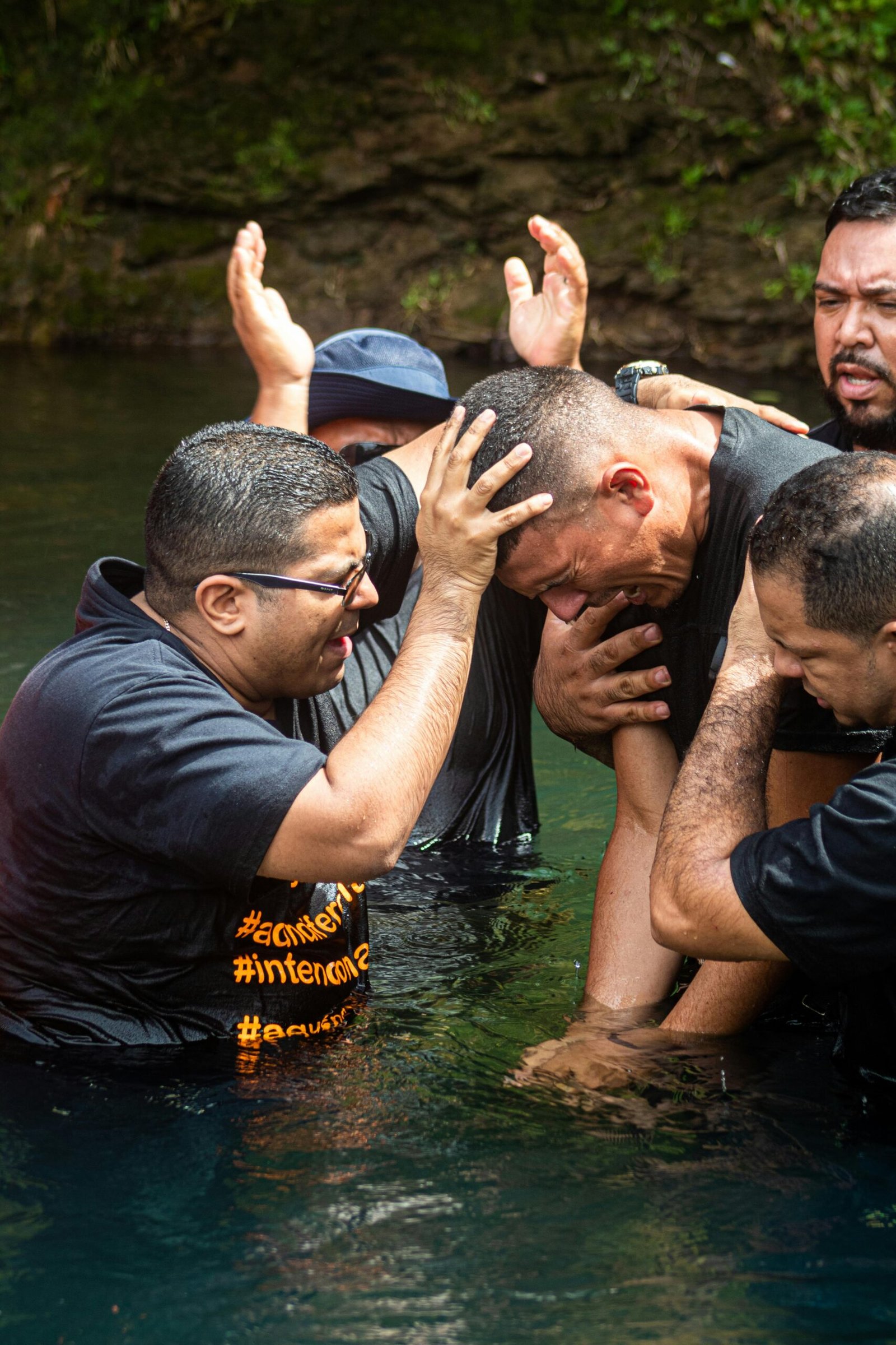 A spiritual baptism ceremony with emotional participants standing waist deep in water.