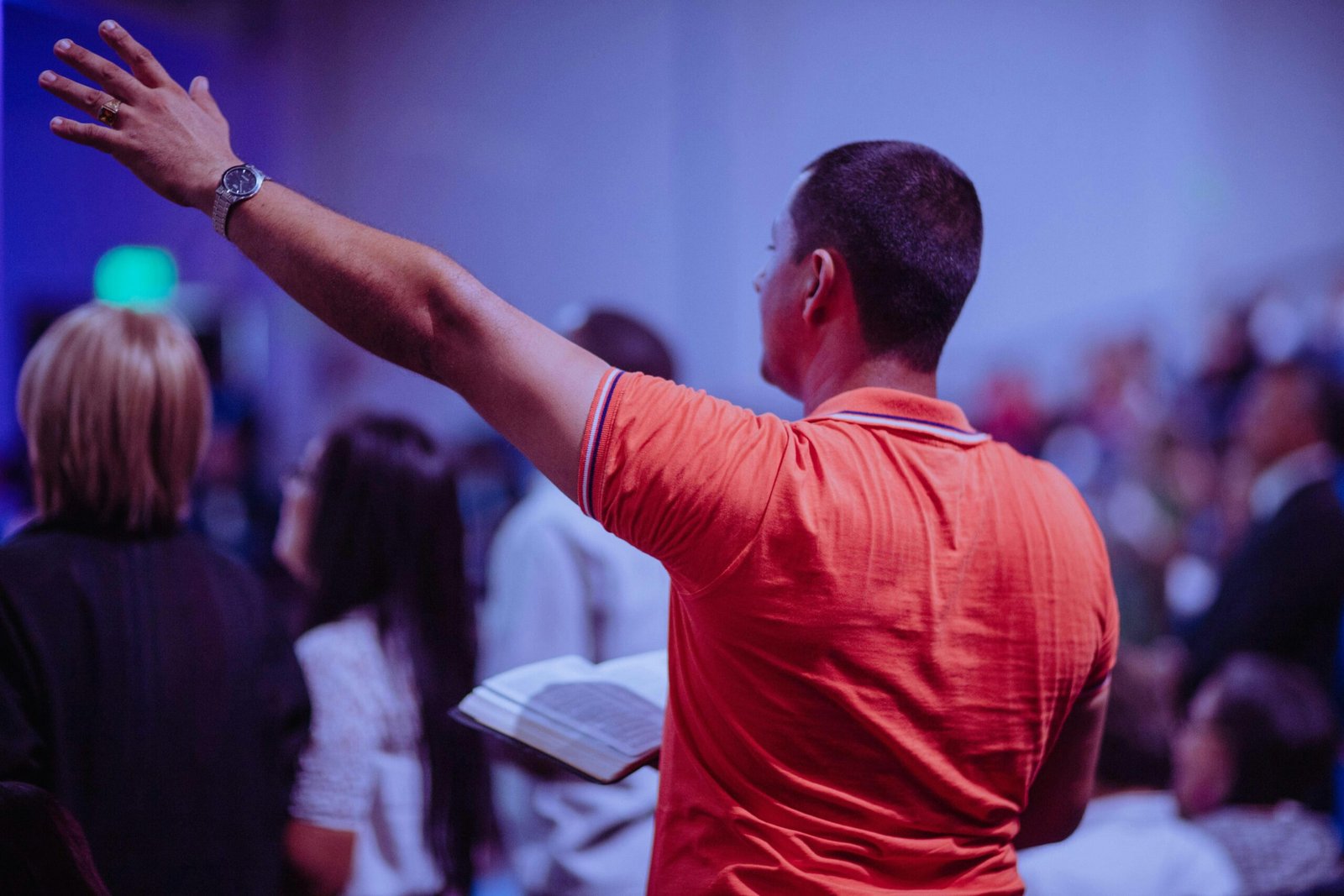 A man worships in a church holding a Bible among a congregation of diverse people.